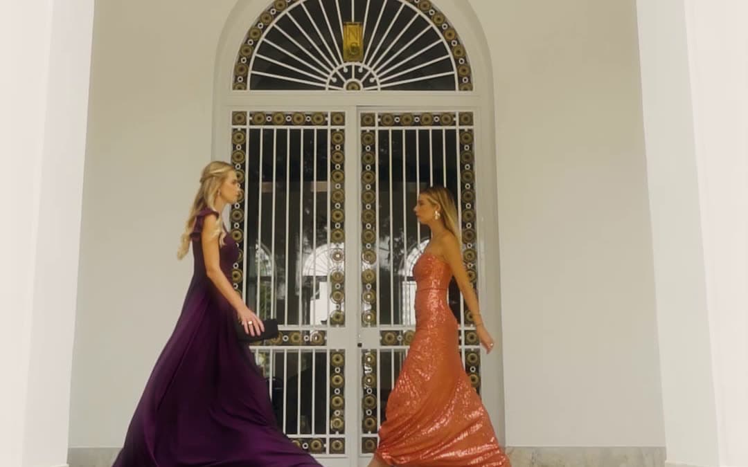 Dois vestidos de festa, um roxo e um coral, sob o arco do casarão